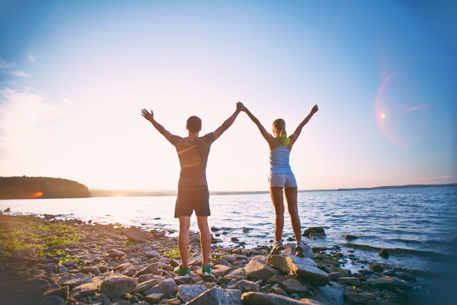 Photo of young sporty couple standing on the coastline with raised arms